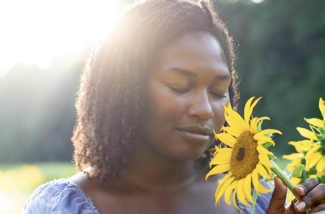 Precious Neely with eyes closed, resting peacefully beside a sunflower in golden light